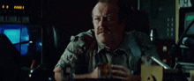 a man with a mustache is sitting at a desk in a dark room in front of a television .