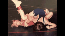 two young boys are wrestling on a mat and one of them is wearing a pink top