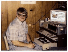 a man wearing glasses sits at a desk with a computer