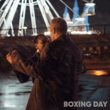 a man and woman are dancing in front of a ferris wheel and the words boxing day are below them