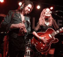 a man playing a guitar next to a woman playing a guitar in front of a sign that says all