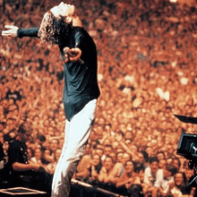 a man singing into a microphone with his arms outstretched in front of a crowd