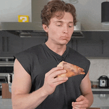 a man in a black shirt is eating a slice of pizza with a yellow question mark in the background