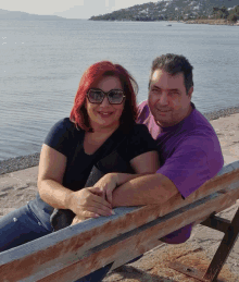 a man and a woman are sitting on a wooden bench by the water