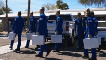 a group of men in blue jumpsuits are carrying briefcases in front of a silver truck that says gmc on the back