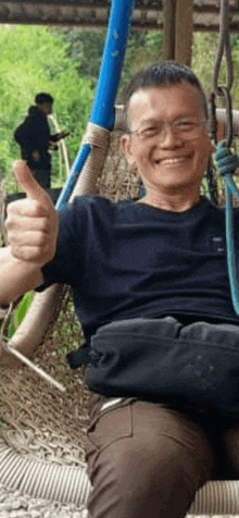 a man is giving a thumbs up while sitting on a hammock .