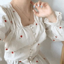 a woman wearing a white dress with red flowers and a necklace