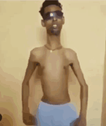 a shirtless man wearing sunglasses and blue shorts is standing in front of a wall .