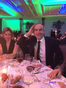 a man in a suit and tie sits at a table with a woman behind him