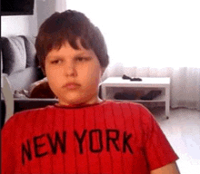 a young boy wearing a red new york t-shirt is looking at the camera .