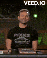 a man wearing a pixies t-shirt is smiling