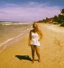 a woman in a white tank top and shorts is standing on a sandy beach