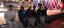 a group of men sit on a sidewalk in front of a sign for light waves