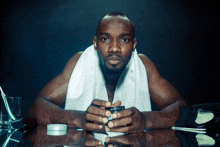 a man with a towel around his neck sits at a table with his hands folded