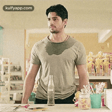 a man in a sweaty shirt is standing in front of a counter with a bottle of soda on it .