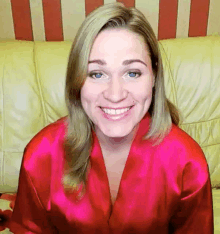 a woman in a red robe is smiling and sitting on a couch