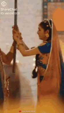 a woman in a sari is holding a man 's hand while standing next to a pole .