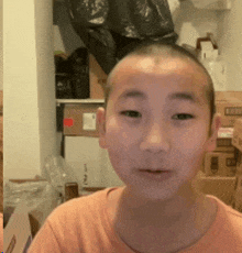 a young boy with a shaved head looks at the camera with boxes in the background