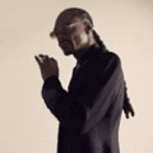 snoop dogg is wearing glasses and a black jacket and is smoking a cigarette .