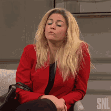 a woman in a red jacket is sitting in a chair with the snl logo on the bottom