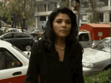 a woman in a black jacket stands in front of a busy street with a building that says iran on it