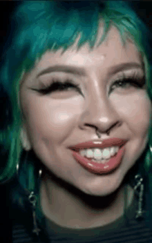 a woman with green hair and a nose ring is smiling and making a funny face .