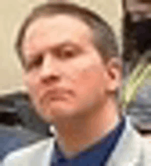 a close up of a man 's face wearing a white jacket and a blue shirt .