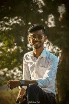 a young man wearing sunglasses and a white shirt is sitting in front of a blurred background that says pixels perfect