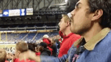 a man in a blue jacket stands in a crowded stadium with a sign that says ' coca cola ' on it