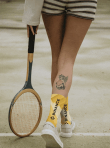 a woman holding a tennis racquet and wearing socks that say binance