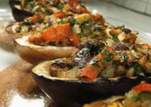 a row of stuffed eggplant bowls filled with vegetables are sitting on a table .