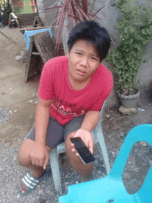 a young boy wearing a red shirt that says ' galaxy ' on it sits on a chair holding a cell phone