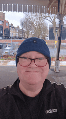 a man wearing glasses and a blue beanie is wearing an adidas jacket