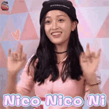 a woman wearing a pink shirt and a black hat is smiling and making a peace sign with her hands .