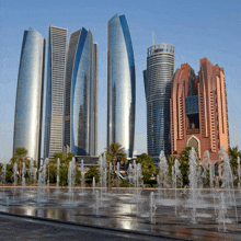 a city skyline with a fountain in the foreground and a building with the word dubai on it