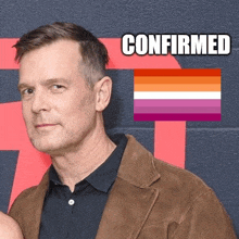 a man in a brown jacket is standing in front of a lesbian flag with the word confirmed above him