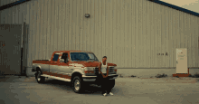 a man stands next to a red and silver pickup truck in front of a building that says 1318 a on it