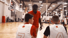 a man in a red shirt is talking to two boys on a basketball court with the number 7 on their jersey