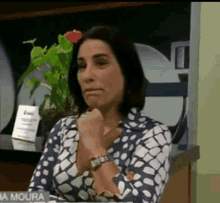 a woman in a blue and white polka dot shirt is sitting at a table with her hands on her chin .