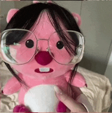 a person is holding a pink stuffed animal with glasses on it .