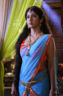 a woman in a blue and red saree with the word madhu on the bottom right