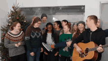 a group of people are posing for a picture in front of a christmas tree and a man is playing a guitar