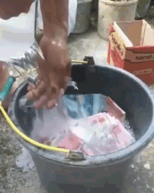 a person is washing their hands in a bucket of water with a box in the background that says sarawak