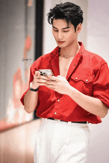 a man wearing a red shirt and white pants is looking at his phone