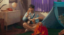 a man is sitting on the floor playing a guitar and talking on a cell phone .