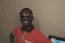 a man wearing sunglasses and a red shirt is smiling and looking at the camera .