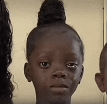 a little girl with her hair in a bun is looking at the camera .