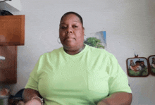 a woman in a bright green shirt is sitting in front of a wall with pictures on it