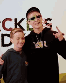 a boy wearing sunglasses stands next to another boy in front of a sign that says rock 'n ' day