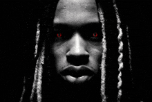 a close up of a man 's face with dreadlocks and red eyes